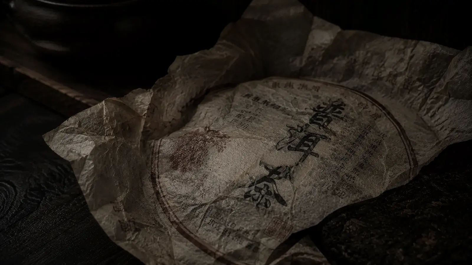 Close-up of a traditional pu-erh tea cake wrapper showing Chinese characters and a neifei ticket on aged, warm-toned paper.
